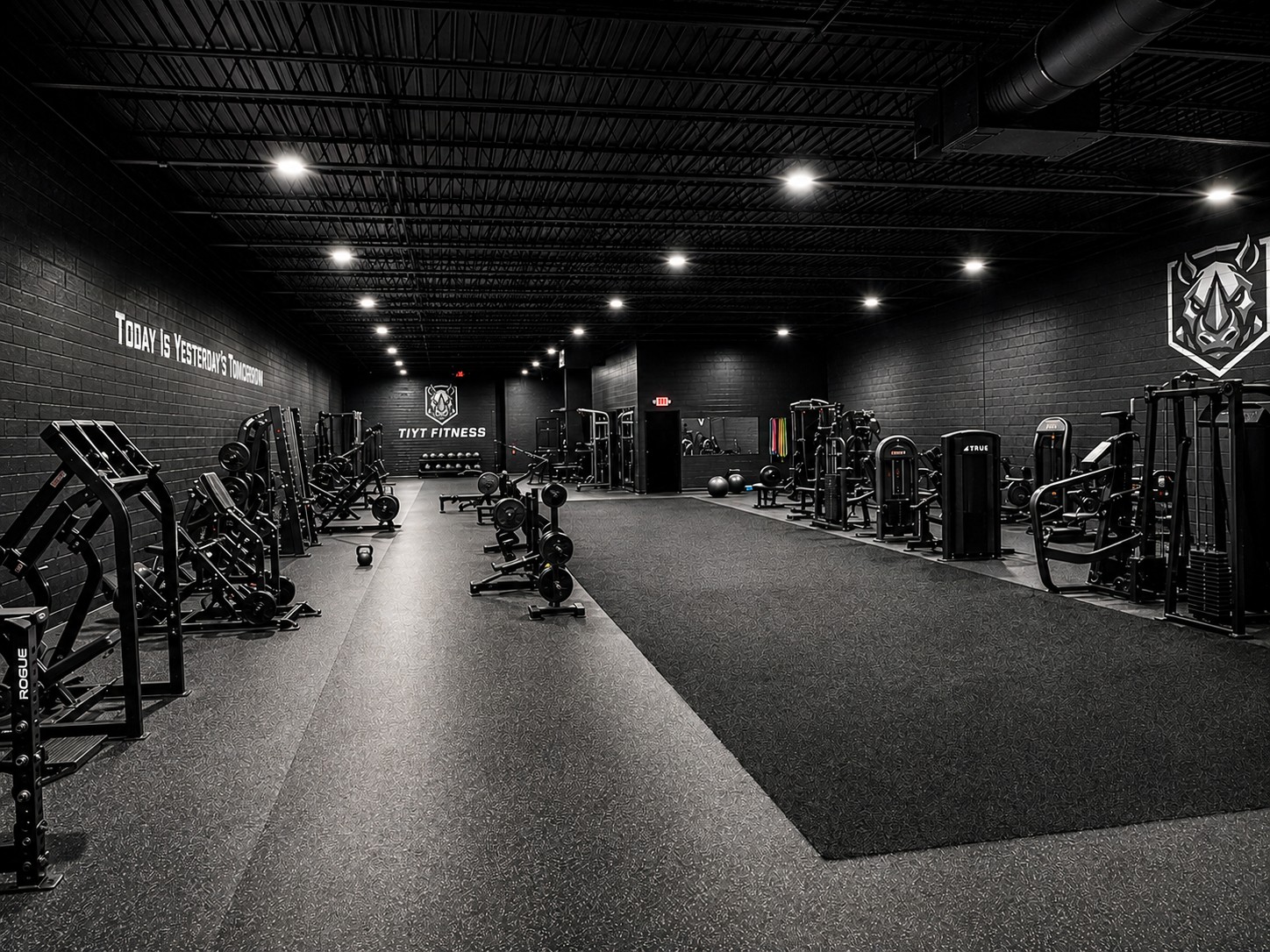 A wide view down the length of the TIYT training floor, lined with squat racks, benches, plate-loaded machines and cardio equipment under rows of overhead lights.